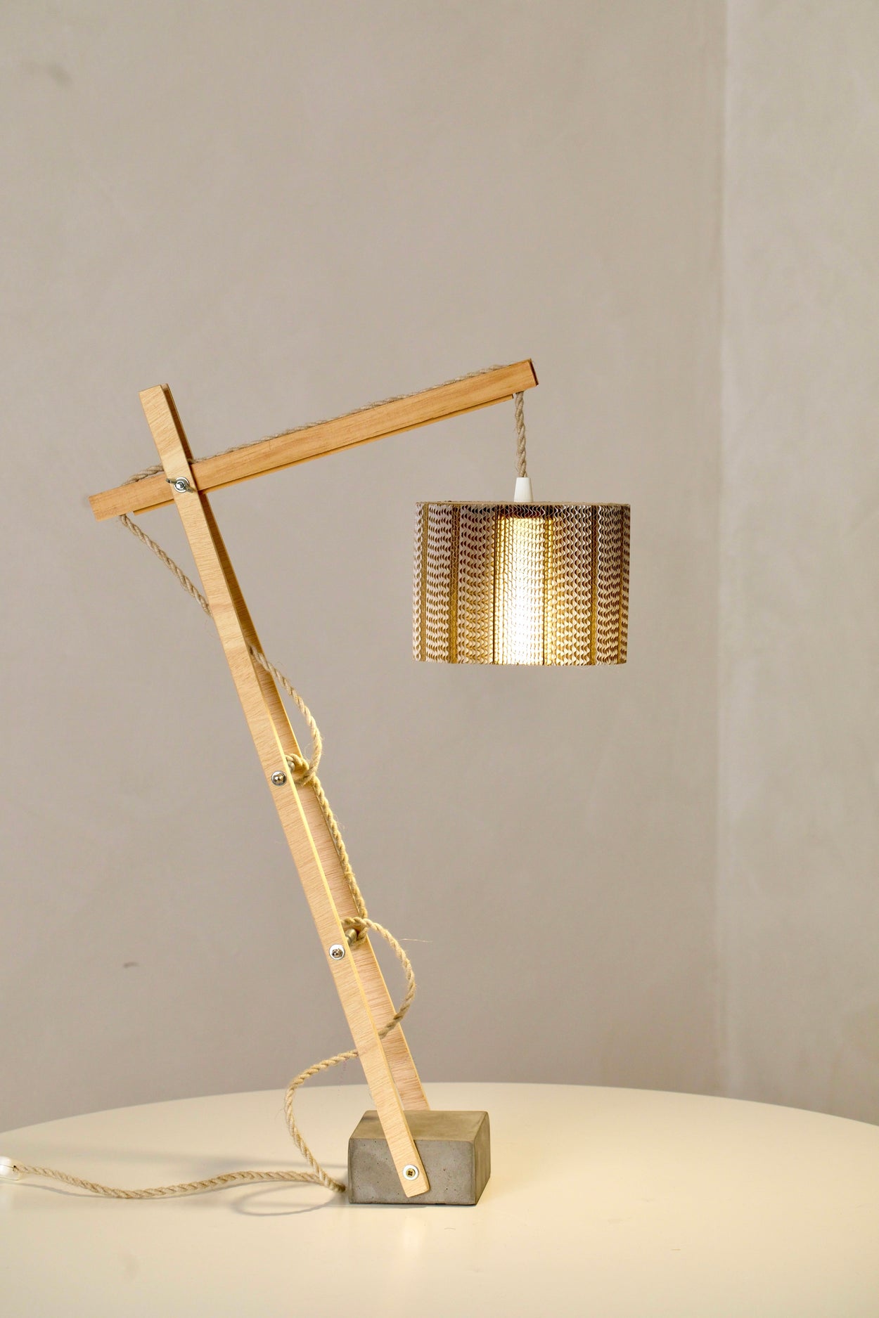 Lámpara de sobremesa con pantalla cilíndrica de cartón ondulado y base de madera  articulada.