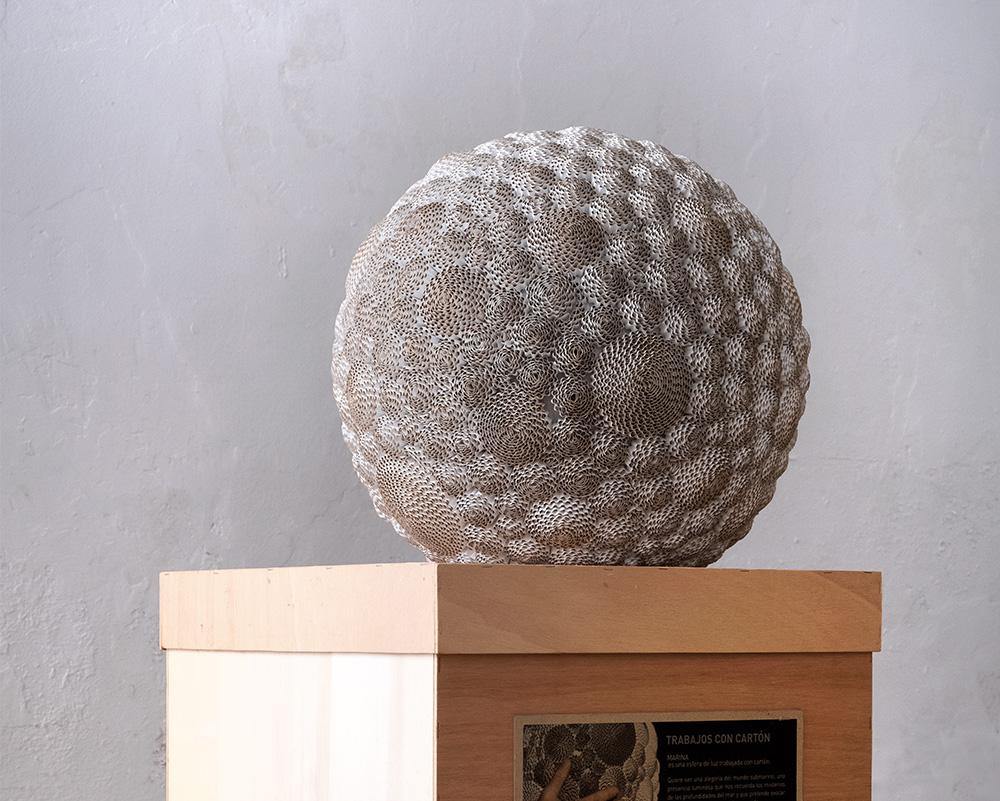 La esféra apagada es una escultura  con patrones circulares que destacan la intrincada estructura del cartón.